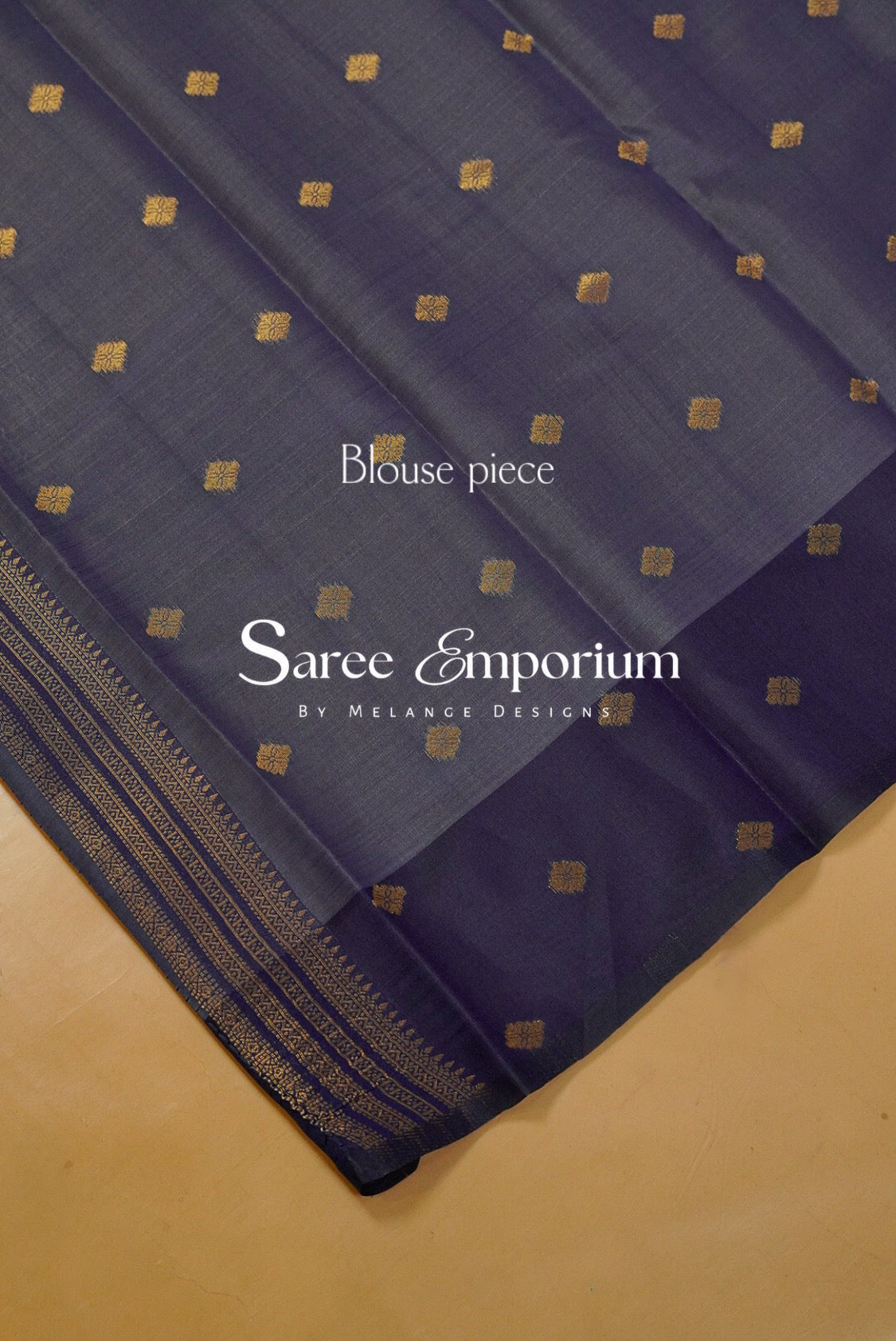 A dark navy blue saree blouse piece with small gold square motifs and a gold border, displayed diagonally on a beige surface.