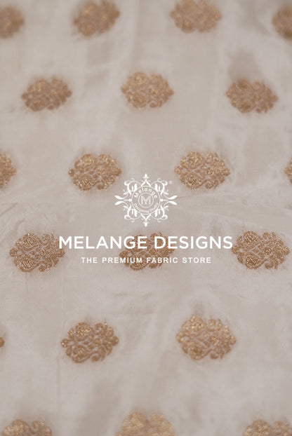 A close-up of a cream-colored Silk Brocade Dyeable Fabric  with repeating metallic gold floral motifs.