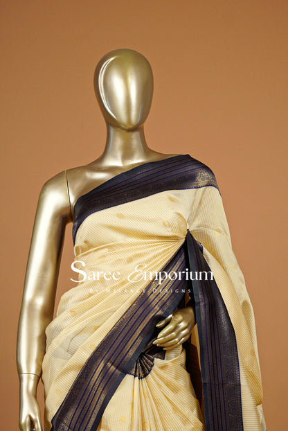 A cream-colored saree with a dark navy blue border and subtle gold motifs.