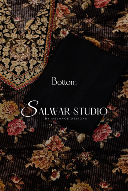 A folded black fabric piece labeled 'Bottom' lies on top of a dark floral printed textile with ornate gold embroidery .