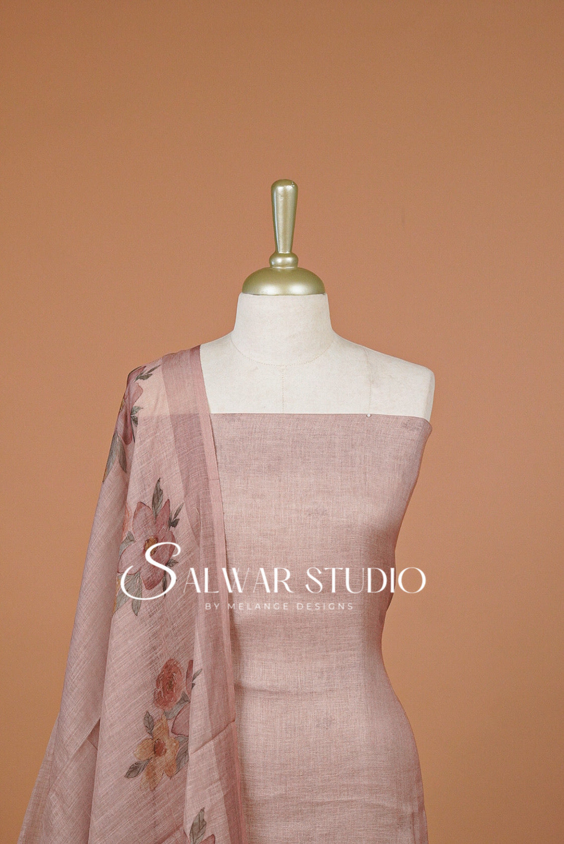 A dusty rose linen salwar suit set displayed on a white mannequin torso, featuring a solid linen tunic and a matching printed dupatta with floral motifs.