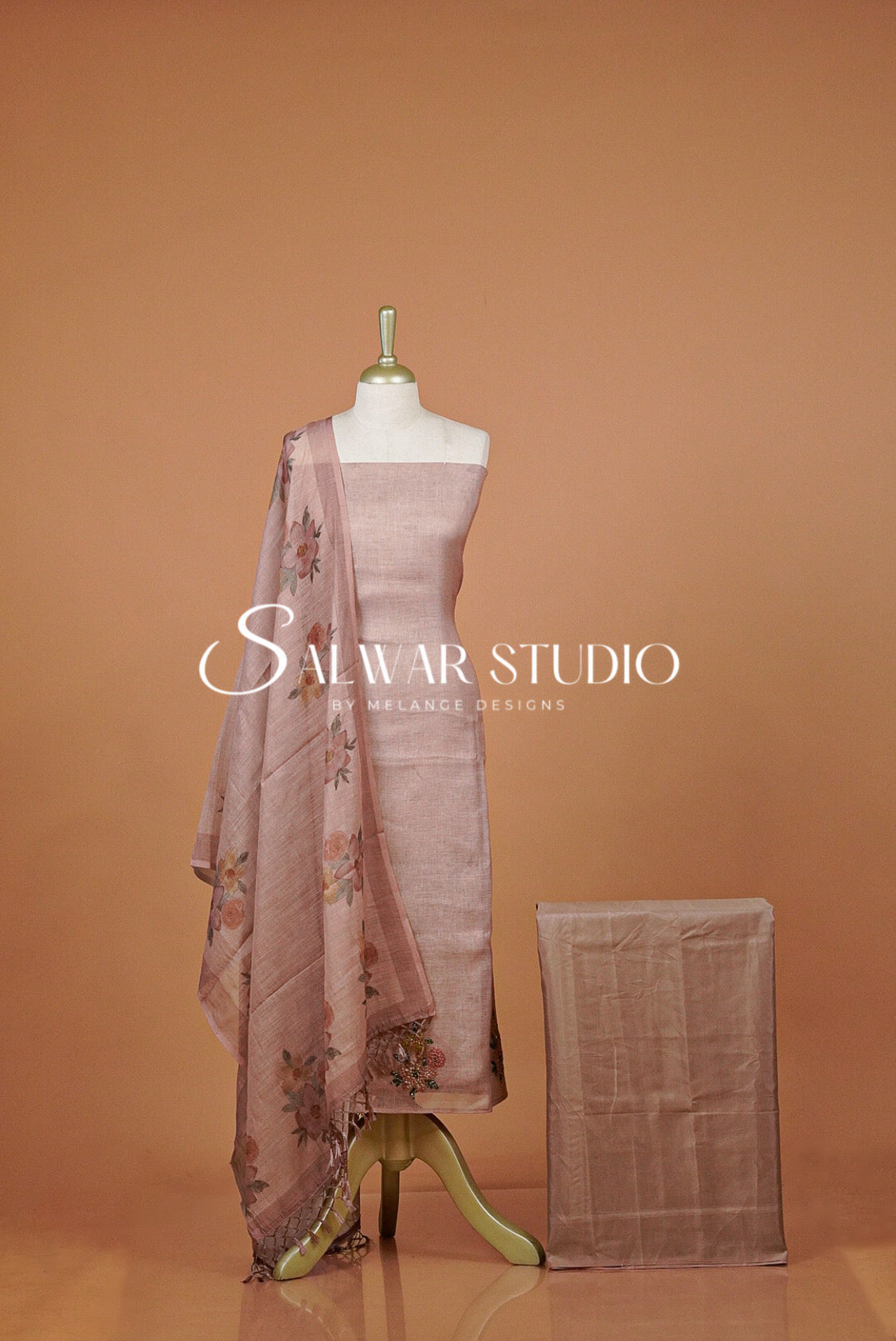 A dusty pink salwar suit set  featuring a kurta, dupatta with floral embroidery, and a matching folded fabric piece.
