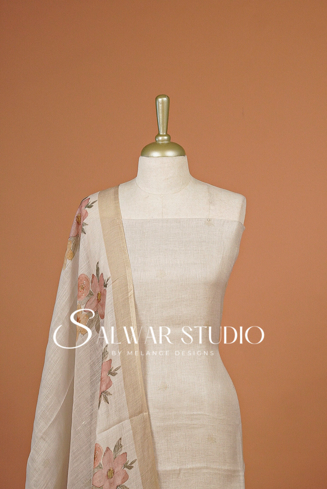An off-white linen salwar suit set The set includes a linen kurta, matching trousers, and a floral printed dupatta with pink and green flowers.
