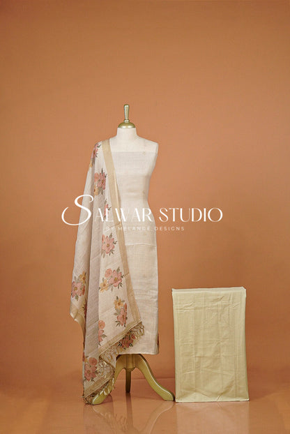 A cream-colored cotton fabric set . The set includes a draped dupatta with a pink and green floral pattern, a matching solid cream kurta, and a folded dupatta.