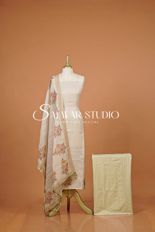 A cream-colored cotton fabric set . The set includes a draped dupatta with a pink and green floral pattern, a matching solid cream kurta, and a folded dupatta.
