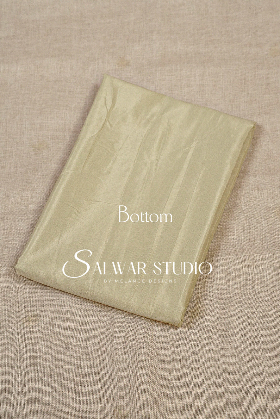 A folded light beige fabric piece, likely a bottom or lining for salwar kameez, The fabric has a subtle sheen and is folded neatly.