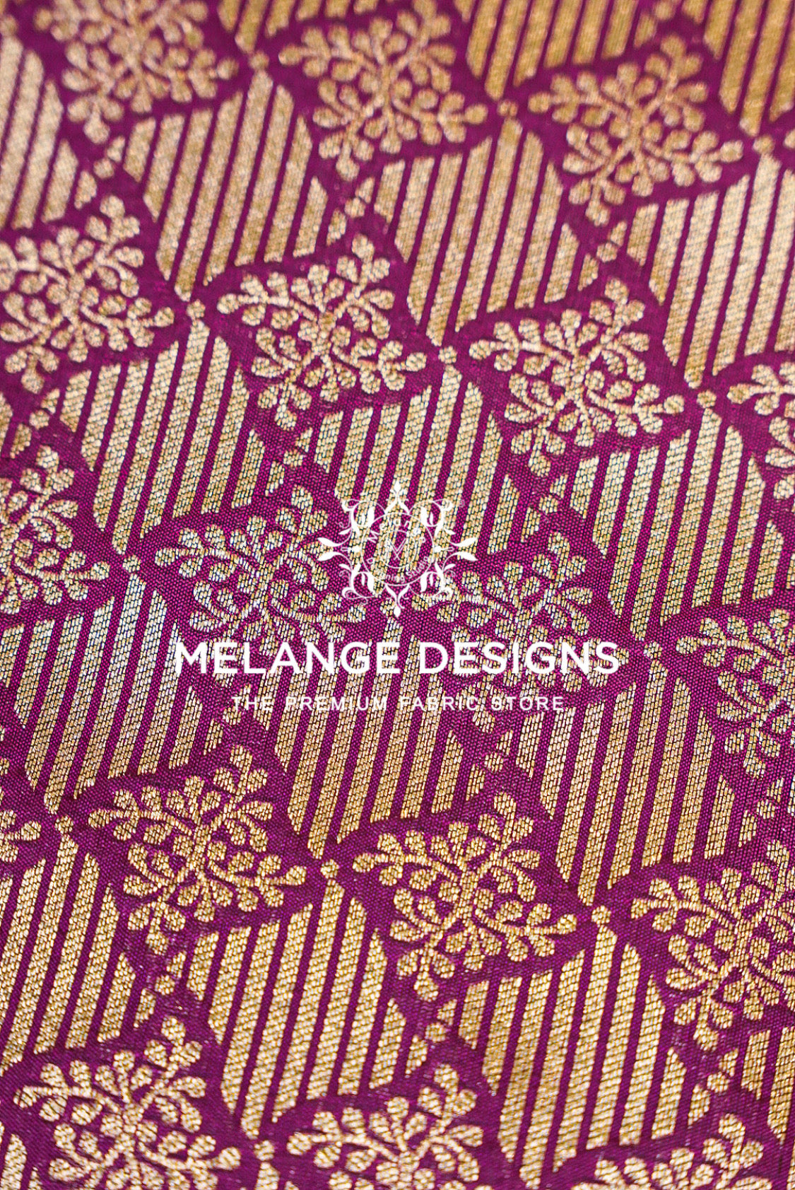 A close-up of a woven Banarasi Brocade Banarasi Brocade Fabric with a rich magenta-purple and gold pattern. The design features vertical gold stripes interwoven with gold floral motifs on a deep purple background.