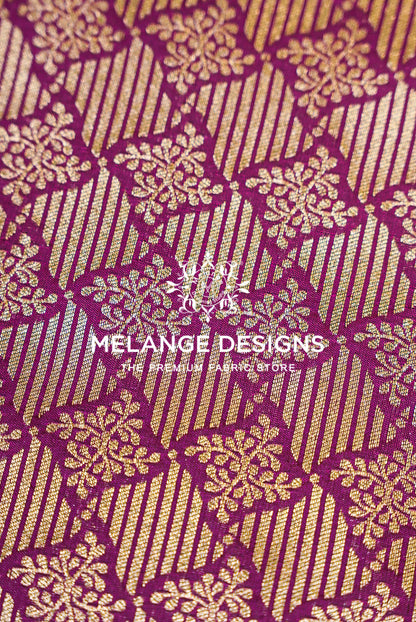 A close-up of a woven Banarasi Brocade Banarasi Brocade Fabric with a rich magenta-purple and gold pattern. The design features vertical gold stripes interwoven with gold floral motifs on a deep purple background.