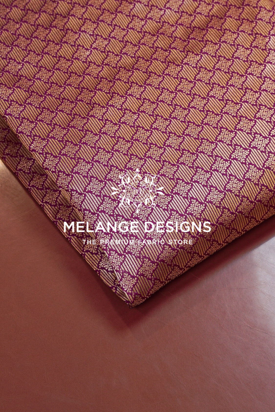 A close-up of folded Banarasi Brocade Banarasi Brocade Fabric with a repeating geometric pattern in metallic gold and deep purple.