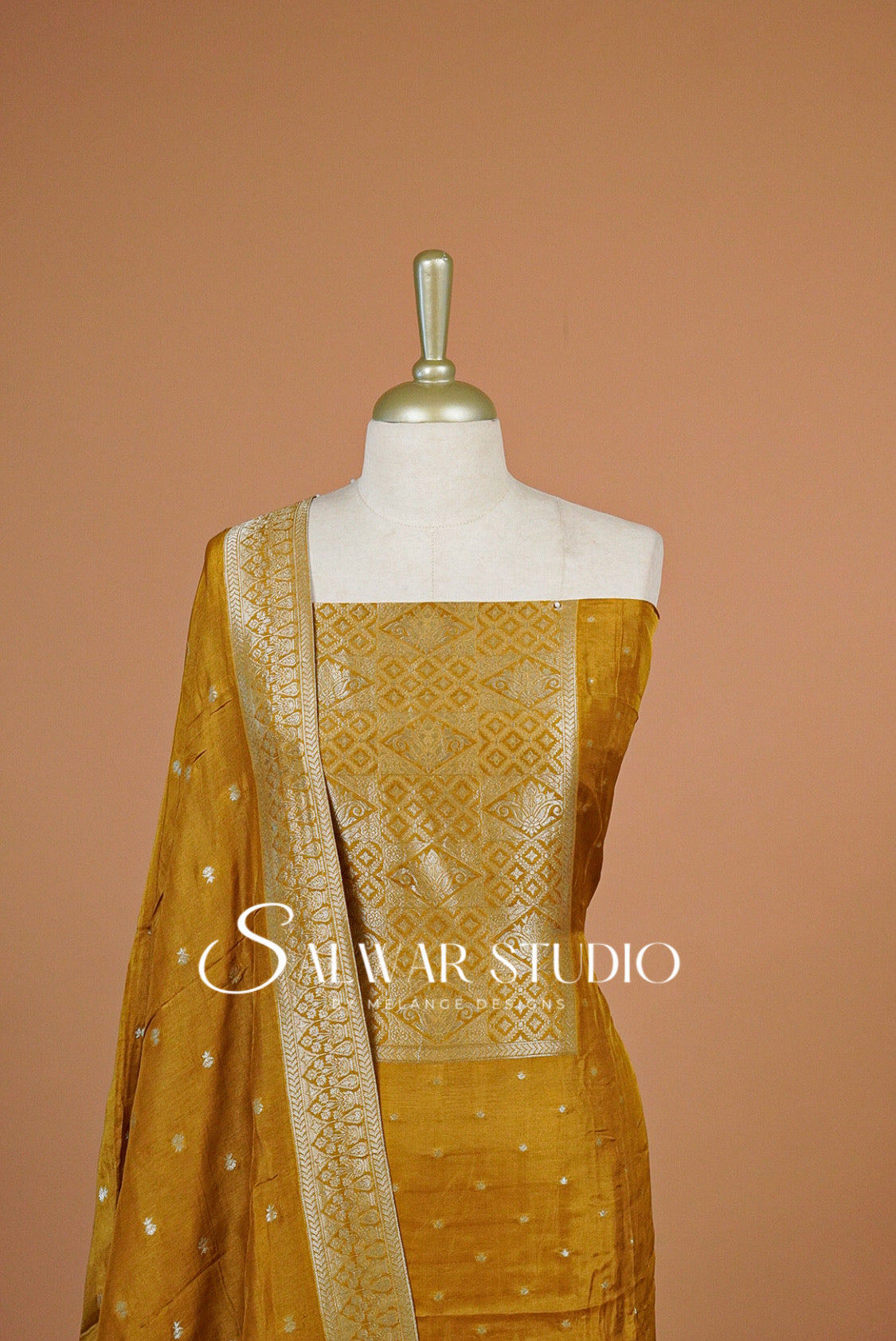 A mustard yellow traditional Indian outfit The set includes a sleeveless blouse with intricate gold zari embroidery, matching skirt, and a draped dupatta with small gold motifs.