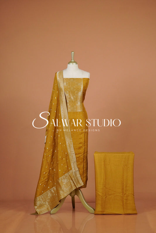 A mustard yellow salwar suit set featuring a kurta, matching bottom, and a dupatta with silver zari embroidery.