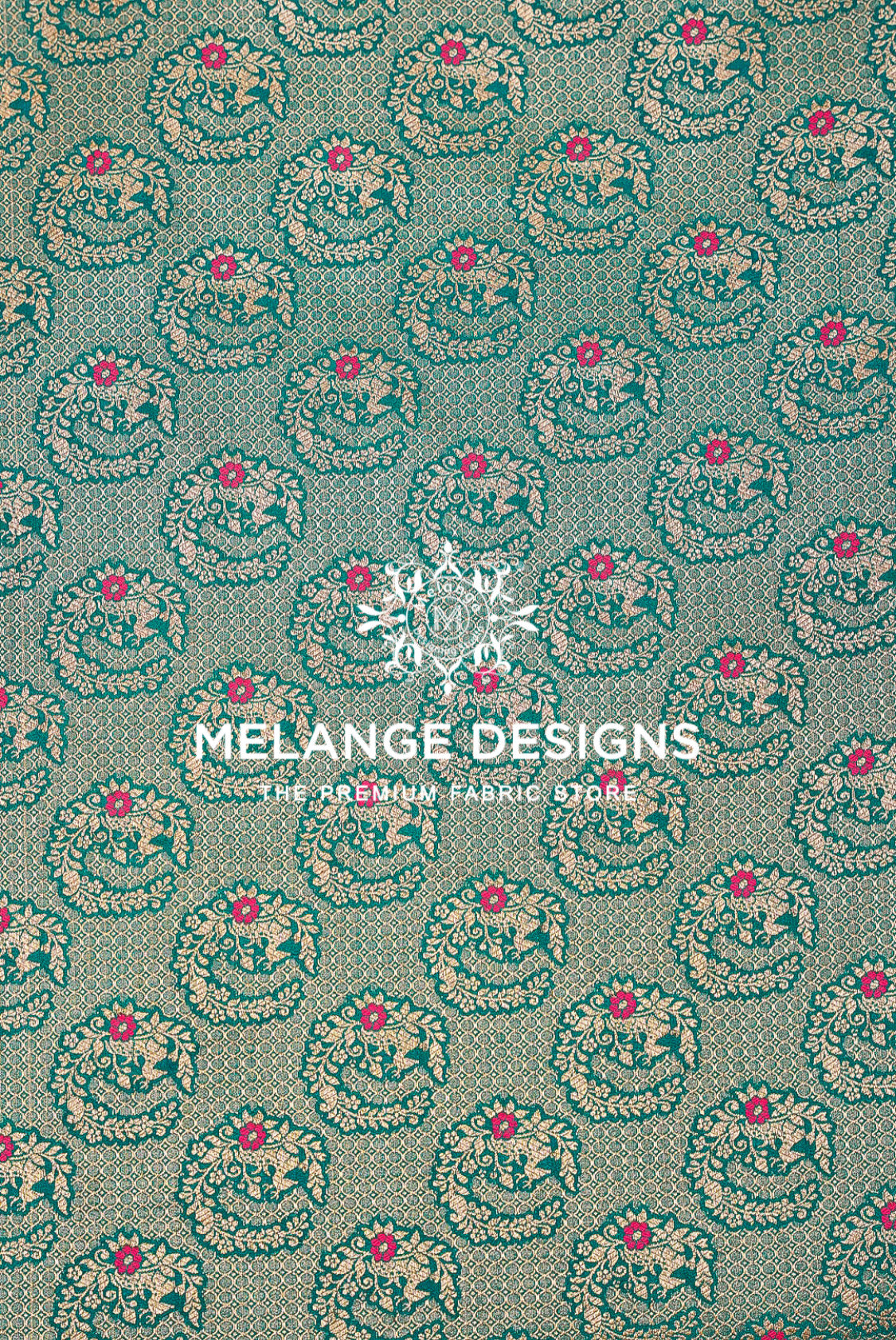 A close-up of patterned Banarasi Silk Brocade Banarasi Silk Brocade Fabric with a repeating teal and beige floral motif and small pink flower accents. 
