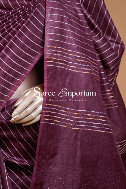 A close-up of a deep plum silk saree with white stripes and gold accents.