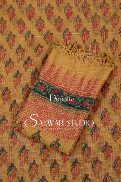 A folded dupatta with a floral block print pattern in red and green on a mustard yellow base, displayed on top of a matching patterned fabric. 
