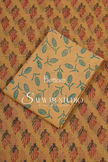 A folded piece of beige fabric with a teal leaf block print pattern, laid diagonally over a larger matching fabric sample showing a red and teal floral block print.