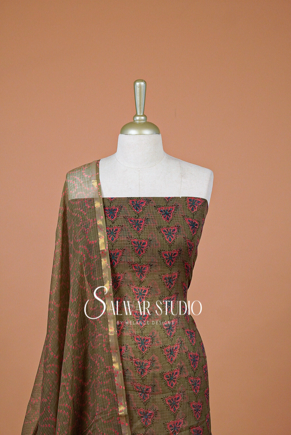 A traditional Indian salwar suit set The set features an olive green salwar fabric with a red and blue floral block print, paired with a matching dupatta that has a gold border and a solid green end piece.