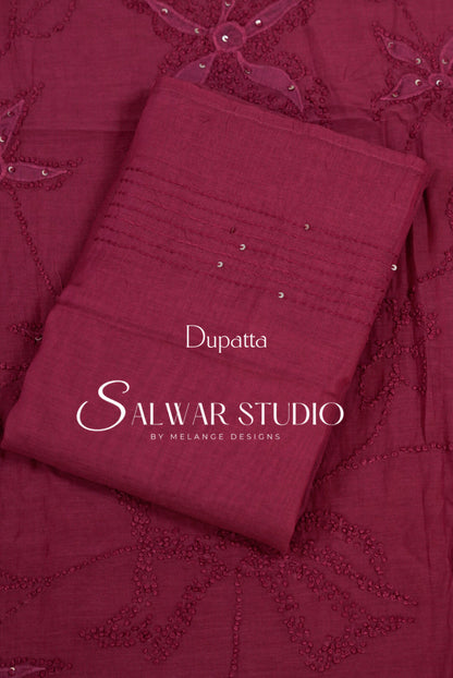 A folded maroon dupatta with embroidered floral patterns and small silver embellishments, matching embroidered fabric . 