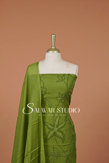 An olive green salwar suit fabric set with floral embroidery. A dupatta is draped over the shoulder.