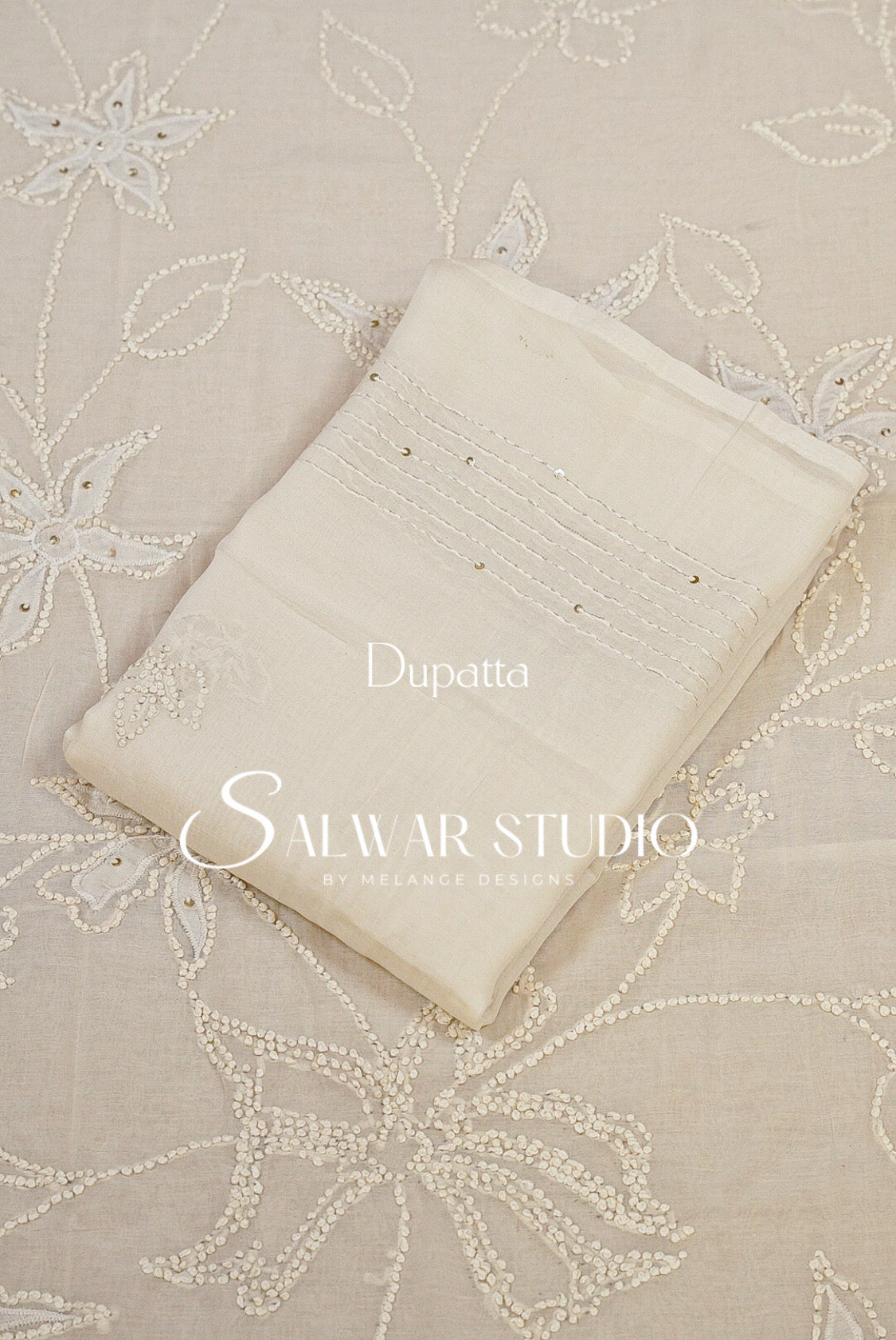 An off-white dupatta with delicate embroidery and beadwork, laid flat on a matching beige embroidered fabric. 