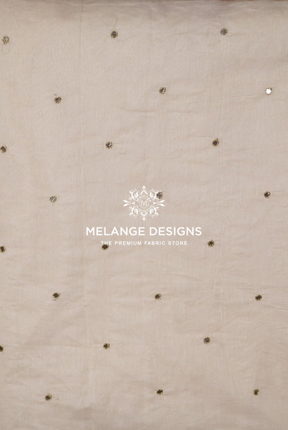Beige Chanderi Glass Work Fabric Dyeable  with scattered small metallic gold and silver embellishments.