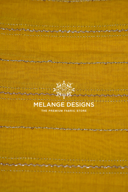 A close-up of a mustard yellow Chanderi Silk Embroidery Fabric  with horizontal metallic silver stitched stripes .