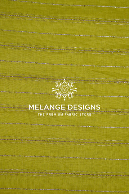 A close-up of a Chanderi Silk Embroidery Fabric sample in a muted olive yellow-green color, featuring horizontal metallic silver stripes.