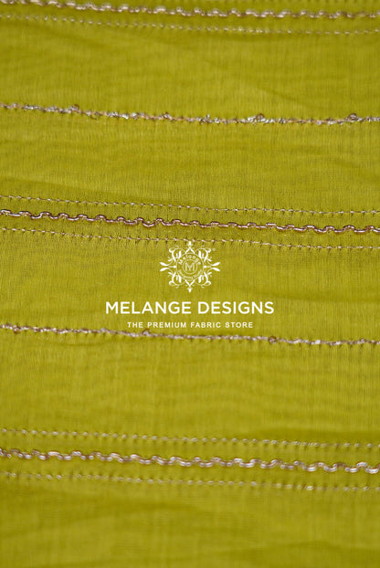 A close-up of a lime green Chanderi Silk Embroidery Fabric with horizontal metallic gold zigzag stitched lines .