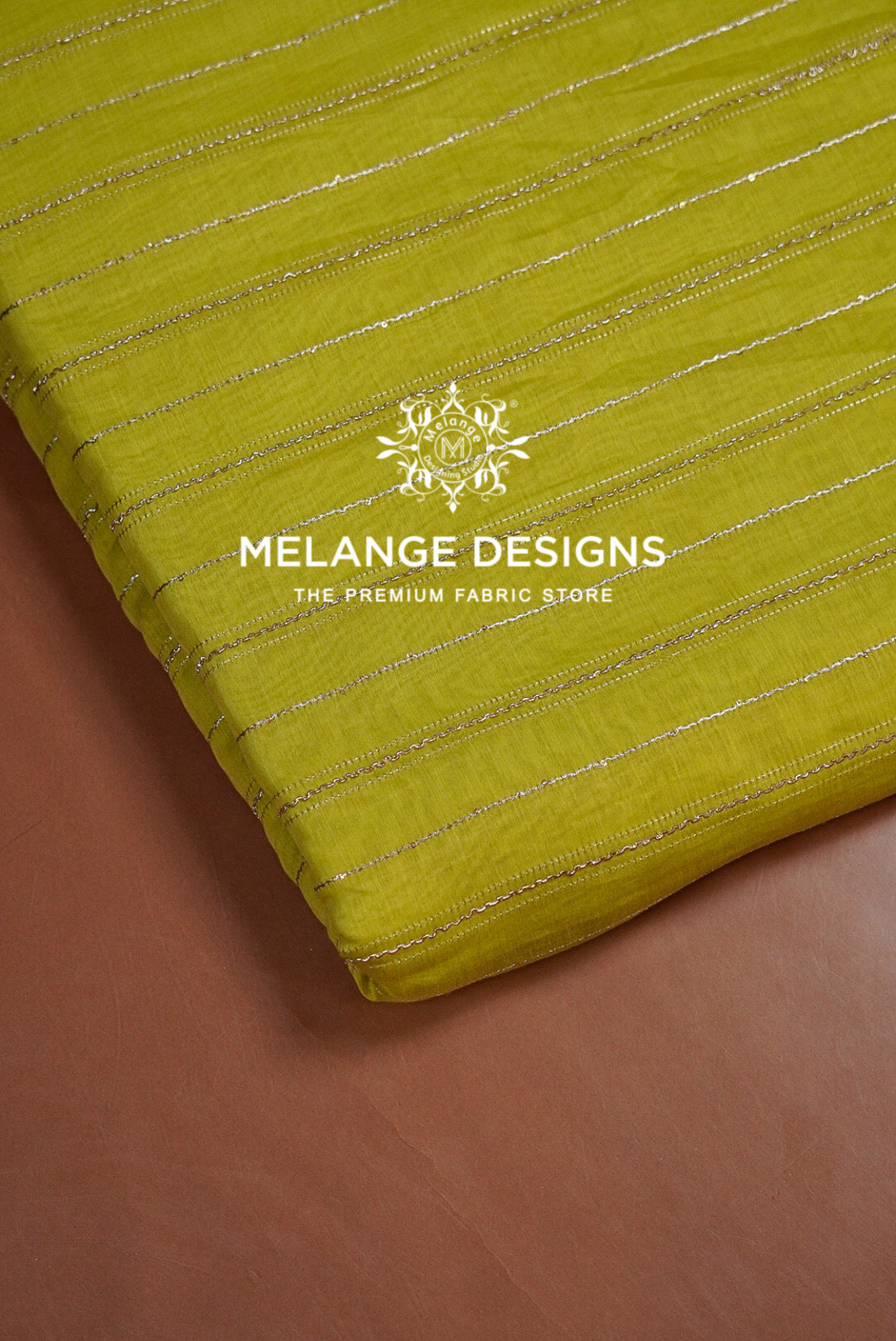 A close-up of a folded olive yellow Chanderi Silk Embroidery Fabric with thin metallic gold stripes.