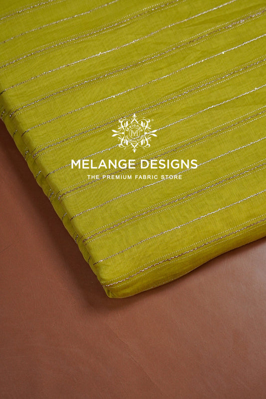 A close-up of a folded olive yellow Chanderi Silk Embroidery Fabric with thin metallic gold stripes.