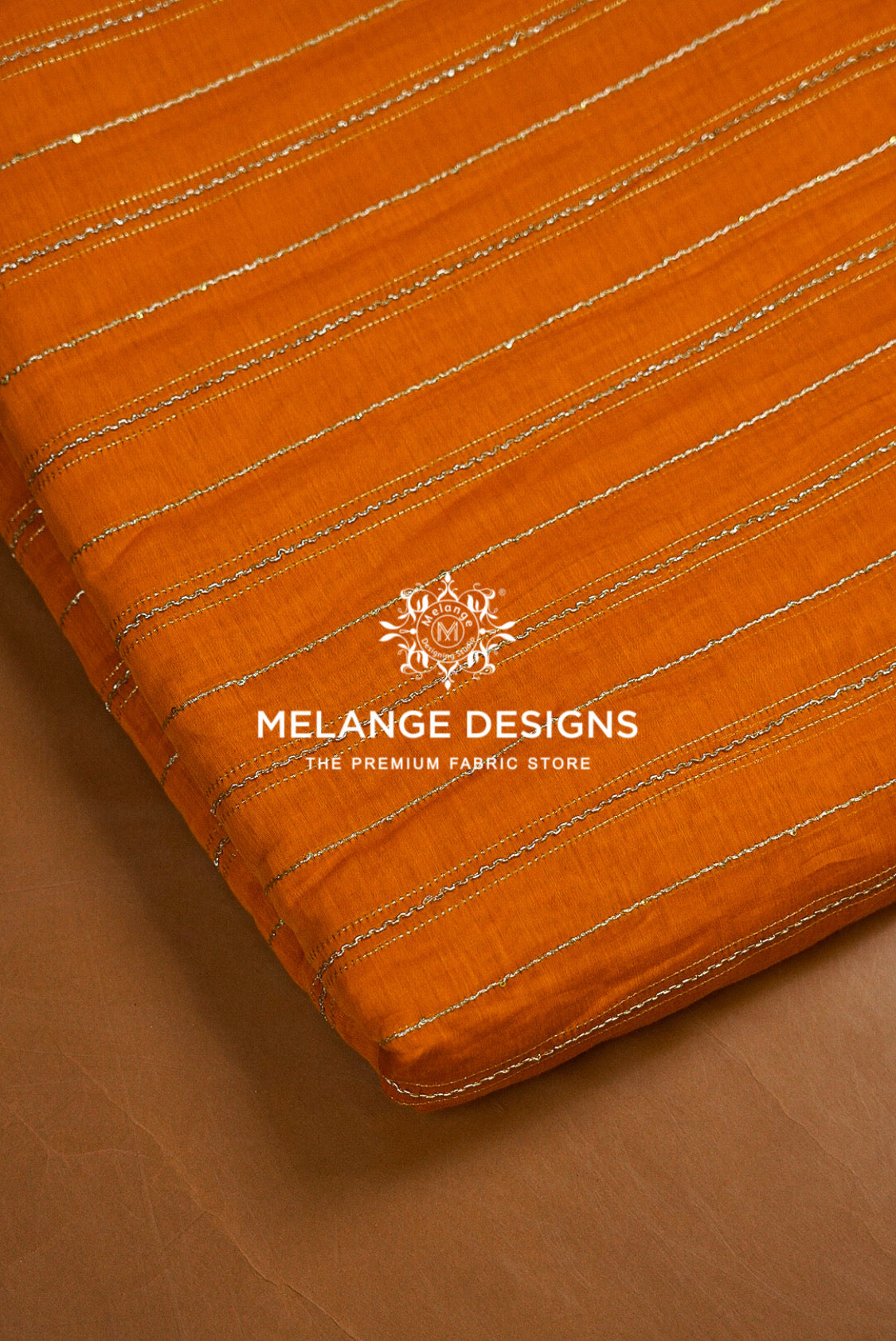A close-up of an orange Chanderi Silk Embroidery Fabric with thin metallic gold stripes, folded over to show its texture and edge. 
