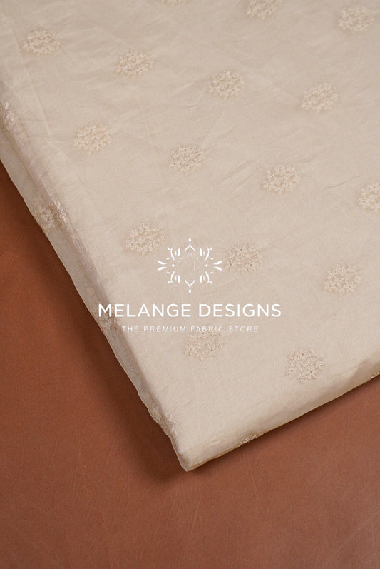 A close-up of a cream-colored CHANDERI SILK EMBROIDERY FABRIC DYEABLE with a subtle floral jacquard pattern.