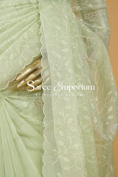 A delicate Kota Embroidery Saree in a refreshing pastel mint-green shade, beautifully detailed with intricate floral embroidery throughout. The sheer, lightweight texture gives it an airy and graceful drape, while the scalloped embroidered border adds a refined feminine finish.