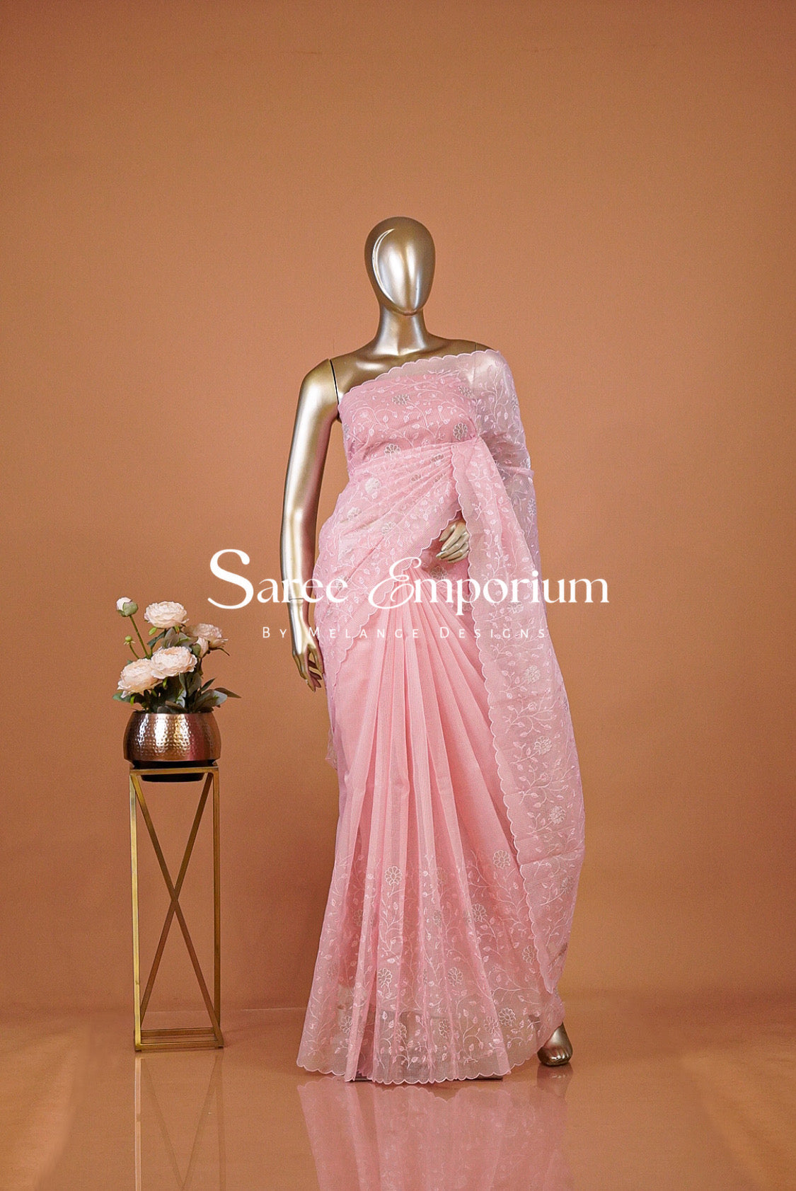 A metallic gold mannequin wearing a light pink embroidered saree,
