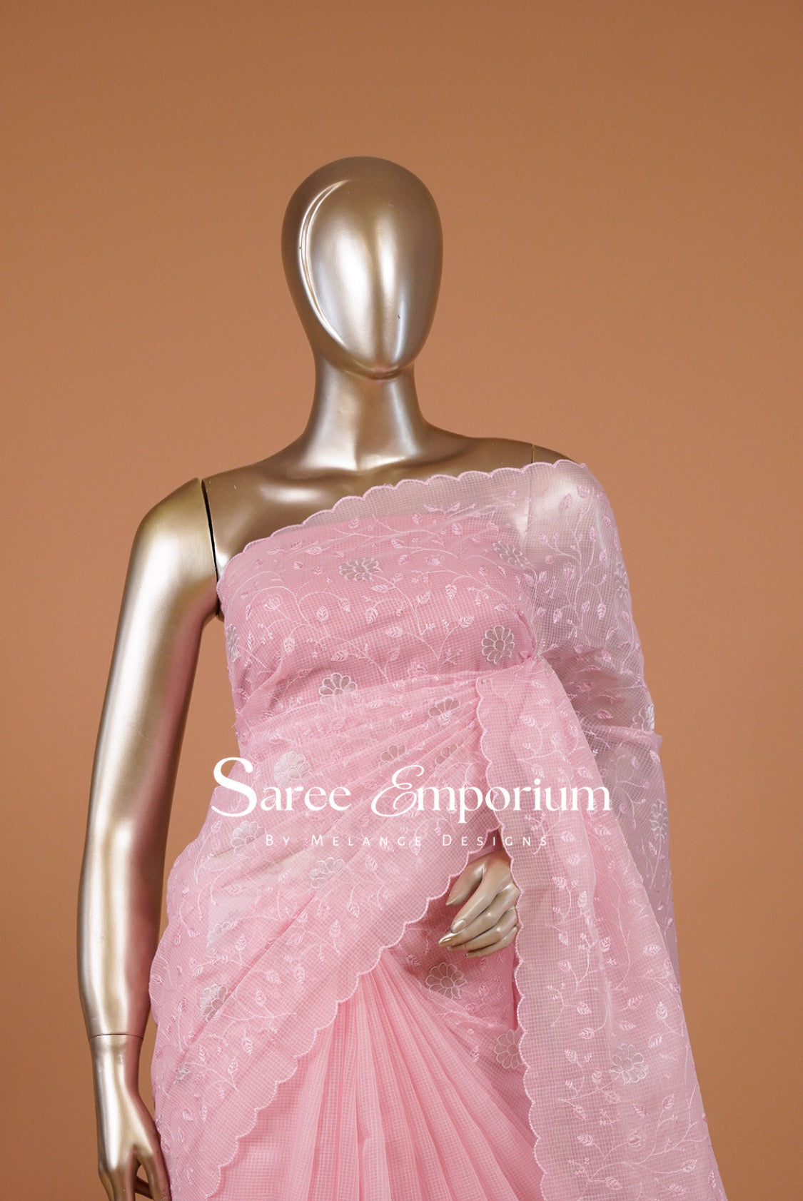 A charming Kota Embroidery Saree in a soft pastel pink shade, beautifully adorned with delicate floral embroidery across the body and pallu. The lightweight, airy texture creates an elegant drape, while the intricately embroidered scalloped border adds a graceful and feminine finish.