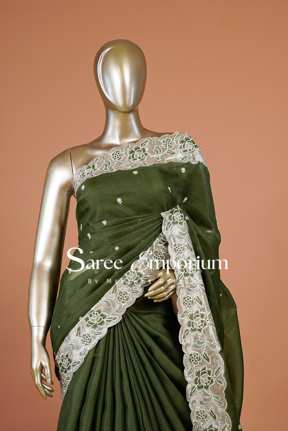 An olive green saree with intricate white floral lace borders and small white embroidered motifs.