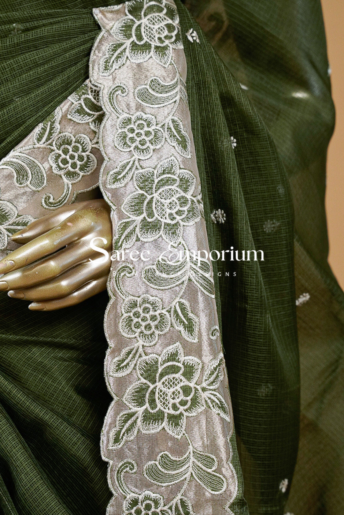 An olive green saree with a wide beige border featuring intricate white floral embroidery.