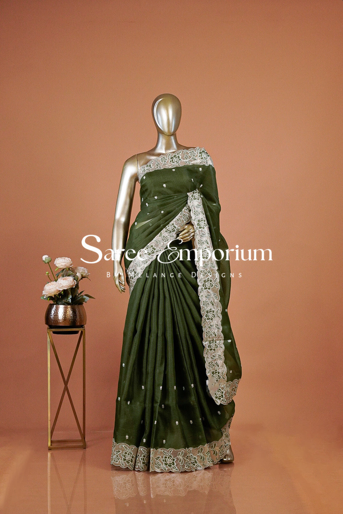 An olive green saree with intricate silver and white floral embroidery . The saree features a solid green body with detailed silver borders and small silver embellishments.