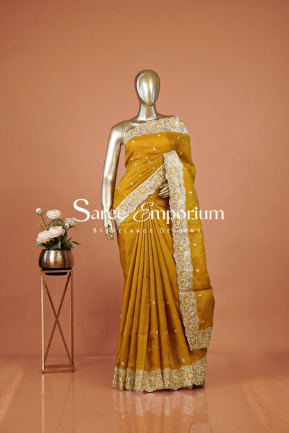 A mustard yellow saree with intricate gold and silver embroidery on the border and pallu.