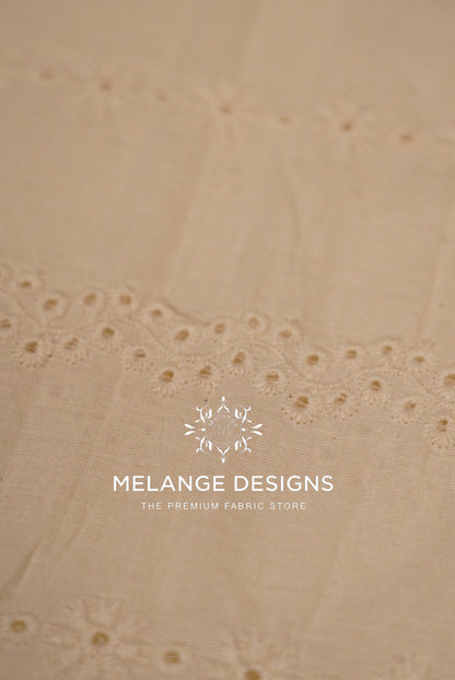 A close-up of a light beige Cotton Hacoba Fabric Dyeable with delicate eyelet embroidery .
