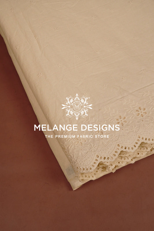 A close-up of a beige Cotton Plazzo Fabric Dyeable sample with floral embroidery and scalloped lace trim.