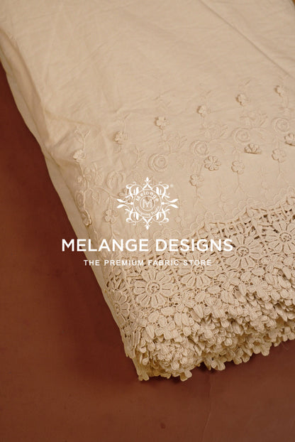 A close-up of a cream-colored Cotton Plazzo Fabric Dyeable with intricate floral embroidery and a decorative lace border.