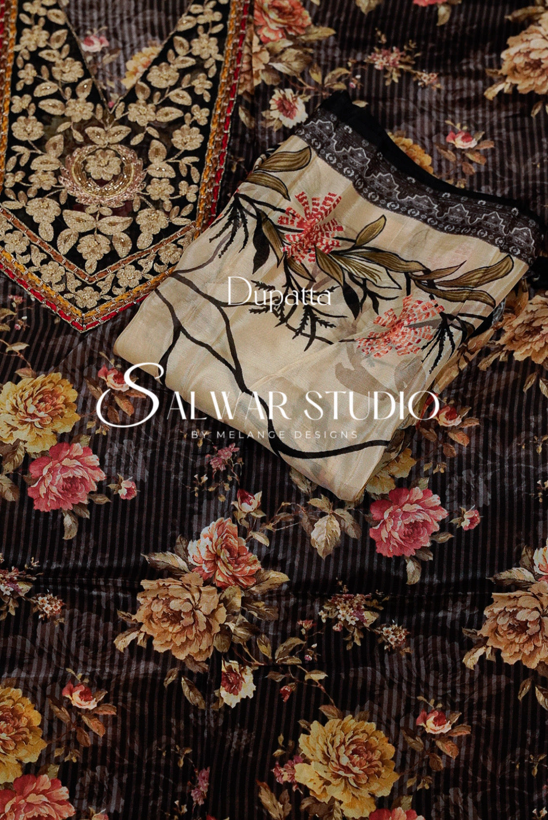 A folded embroidered salwar suit fabric set from Salwar Studio by Molvi Designs, featuring a dark brown floral printed base with a beige embroidered kurta piece layered on top, both decorated with pink and yellow flowers and gold leaf patterns.