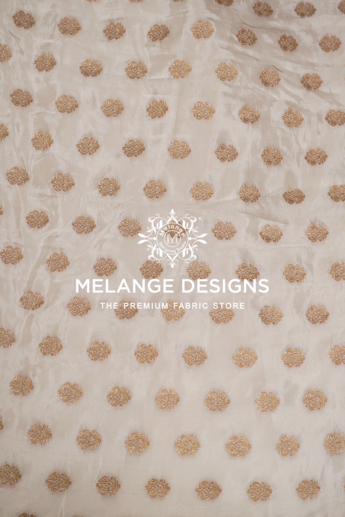 A close-up of a sheer off-white Silk Brocade Dyeable Fabric with a repeating pattern of metallic gold embroidered dots.