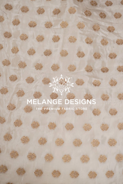A close-up of a sheer off-white Silk Brocade Dyeable Fabric with a repeating pattern of metallic gold embroidered dots.