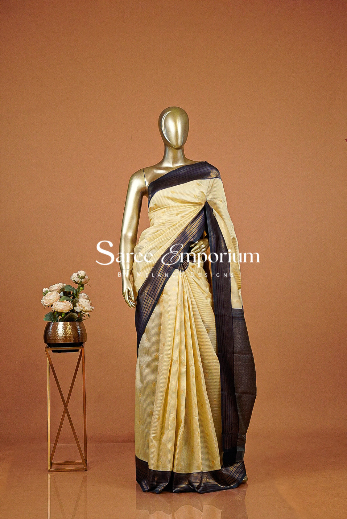 A gold mannequin displays a light beige and dark navy blue saree .