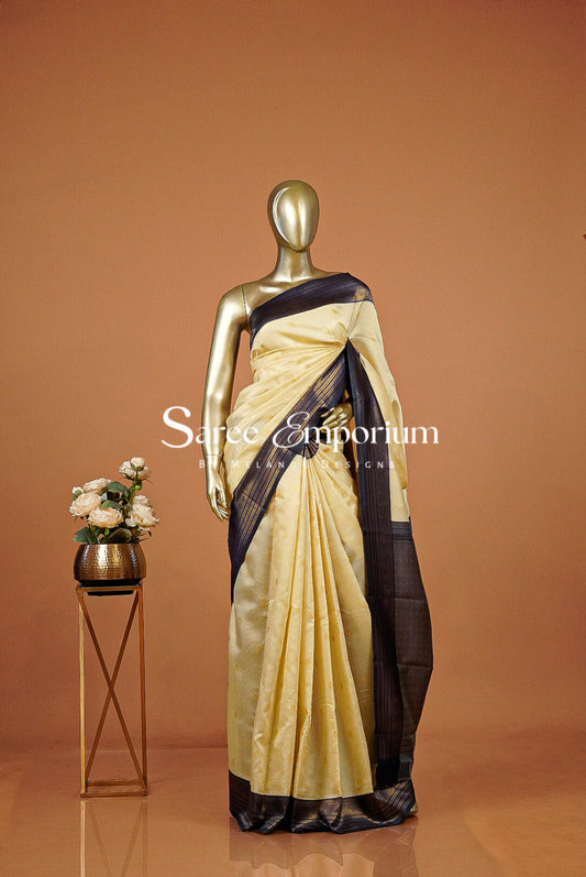 A gold mannequin displays a light beige and dark navy blue saree .