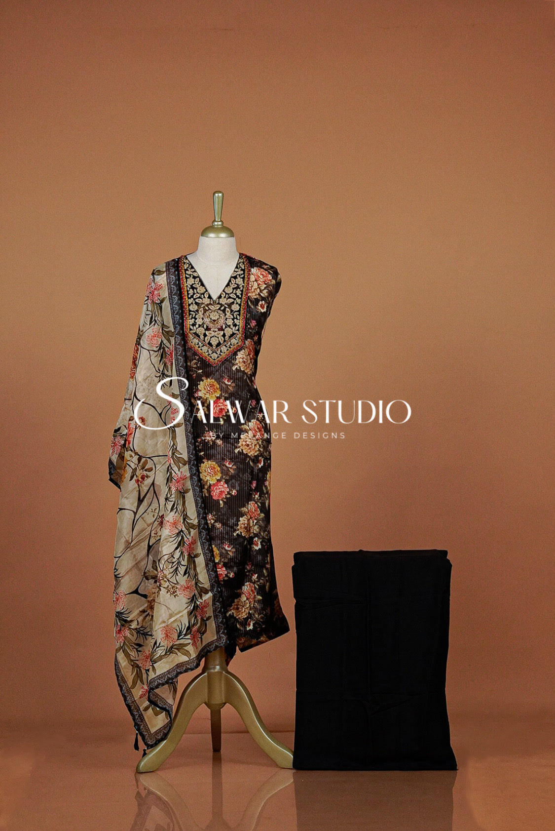 A printed sleeveless kurta displayed on a mannequin with a matching dupatta draped over it, alongside a folded black garment.