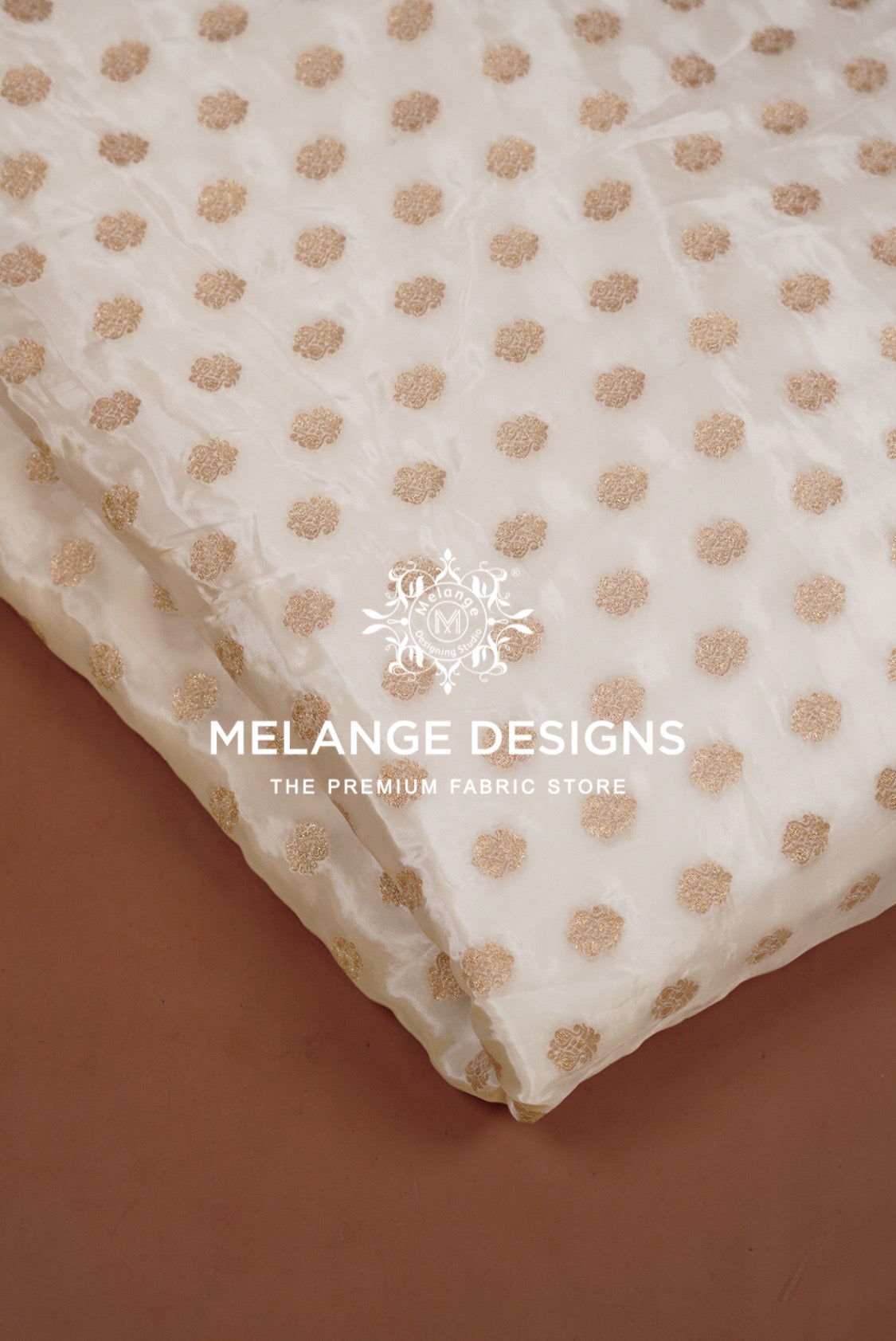 A close-up of a white or cream sheer Silk Brocade Dyeable Fabric  with a repeating metallic gold polka dot pattern.