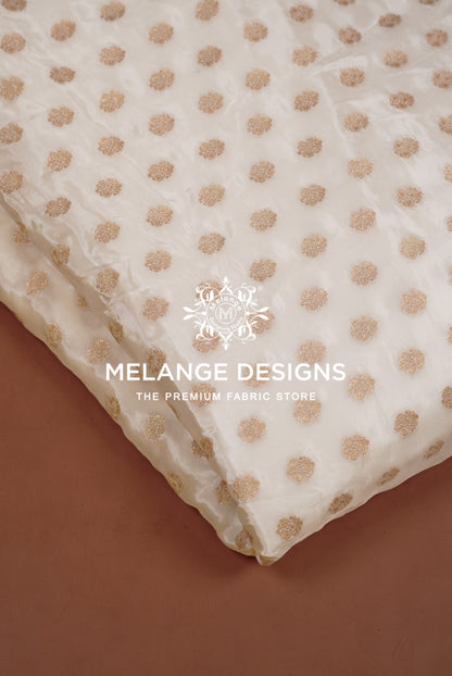 A close-up of a white or cream sheer Silk Brocade Dyeable Fabric  with a repeating metallic gold polka dot pattern.