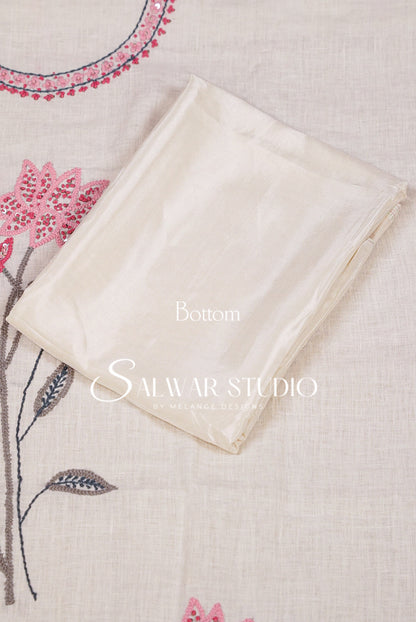 A folded cream-colored fabric panel, labeled 'Bottom' with a 'Salwar Studio' watermark, displayed on a beige linen fabric with pink floral embroidery.